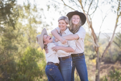 Brother and sister hugging mum laughing on farm in drought - Australian Stock Image