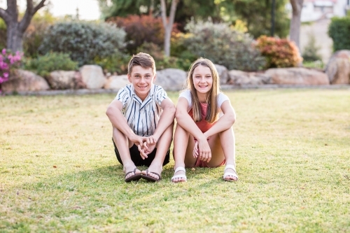 Brother and sister sitting close together resting arms on knees smiling