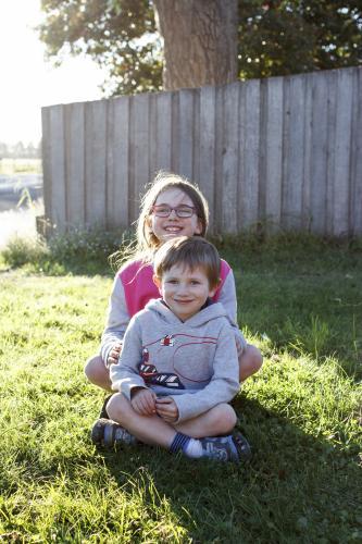 Brother and Sister sitting on green grass in afternoon sun - Australian Stock Image