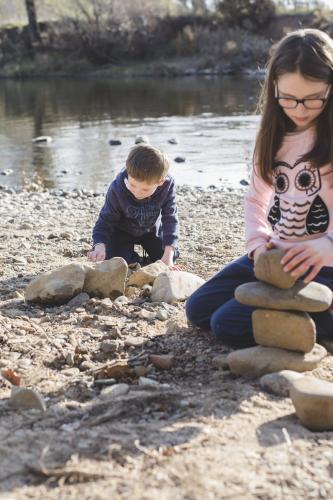 Brother and sister stacking rocks by rivers edge - Australian Stock Image