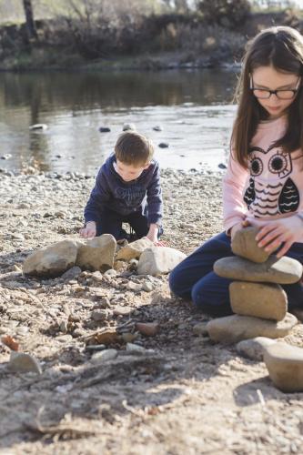 Brother and sister stacking rocks by rivers edge
