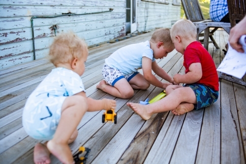 Brothers play with toys on patio deck of weather farm house. - Australian Stock Image
