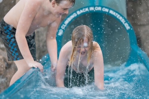 Brothers playing at the bottom of a waterslide on holiday - Australian Stock Image