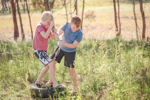 Brothers playing on broken rope swing in natural bush setting - Australian Stock Image