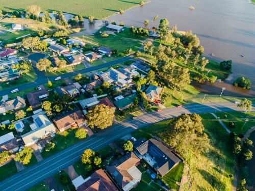 Brown floodwaters backflowing over farmland flooding towards houses - Australian Stock Image