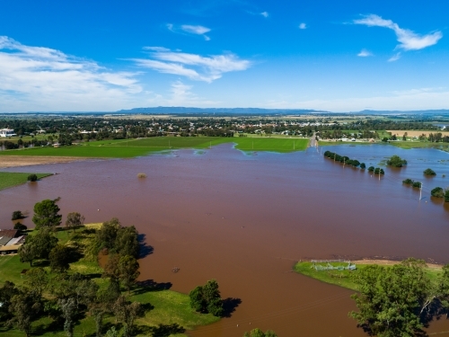 Brown floodwaters over farmland in Singleton in midday sunlight - Australian Stock Image