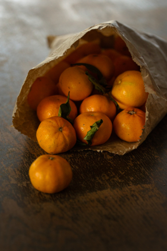 Brown paper bag overflowing with mandarins on wooden table - Australian Stock Image