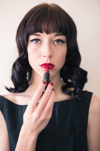 Brunette woman holding red lipstick to her lips - Australian Stock Image