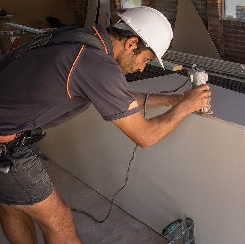 Builder wearing hard hat & tool belt using router on door - Australian Stock Image
