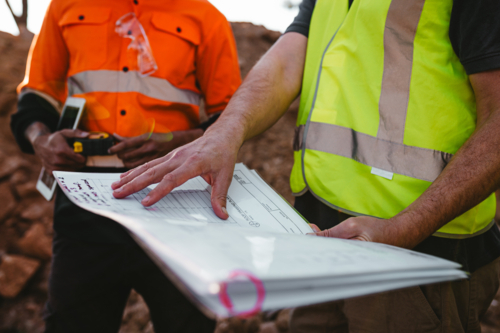 Builders holding a blueprint at the construction site. - Australian Stock Image