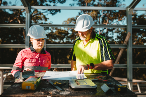 Builders in hardhats looking at the blueprints laid on a flat surface - Australian Stock Image