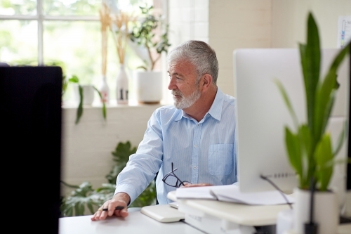 Businessman sitting at a desk in an open office studio - Australian Stock Image