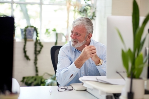 Businessman sitting at a desk in an open office studio - Australian Stock Image