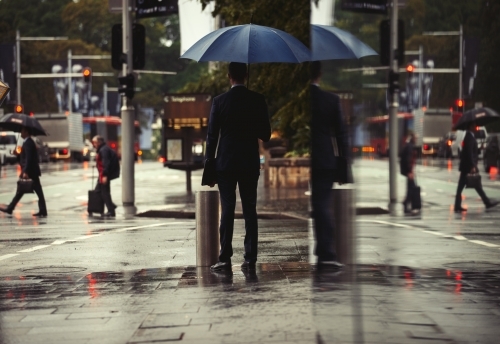 Businessman standing in rain with umbrella - Australian Stock Image