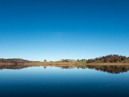 Calm rural water storage dam with a large reflected blue sky