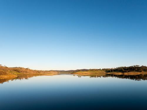 Calm rural water storage dam with a large reflected blue sky - Australian Stock Image