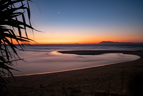 Calm sea with a winding tidal pool reflecting the sky colours - Australian Stock Image