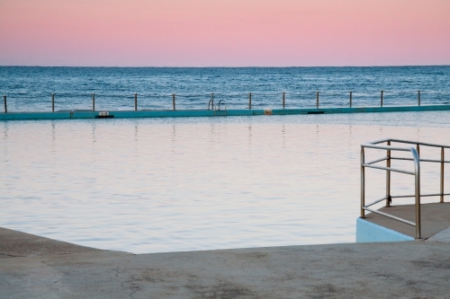 Calm tidal baths next to a choppy sea with pastel colours in the sky - Australian Stock Image