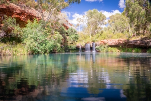Calm waters and a clear reflection in front of a idyllic waterfall on a sunny day - Australian Stock Image