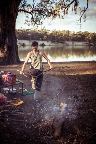 Camping life - female breaking a large stick against her knee to put on the camp fire - Australian Stock Image
