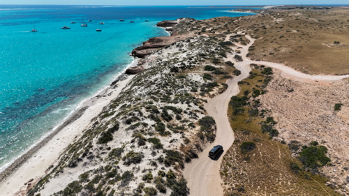 Car driving along windy dirt road next to ocean - Australian Stock Image