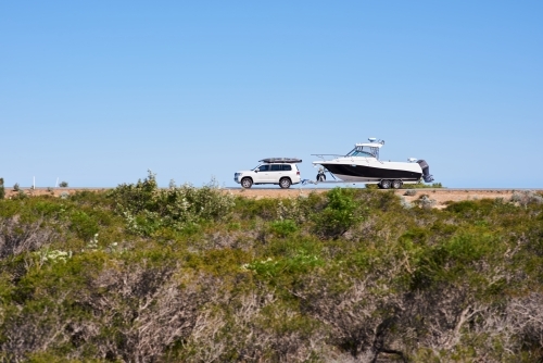 Car towing a boat along a coastal road in Western Australia under blue sky, with motion blur.