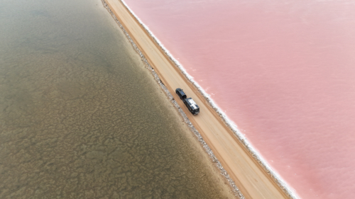 Caravan driving alongside pink salt lake - Australian Stock Image
