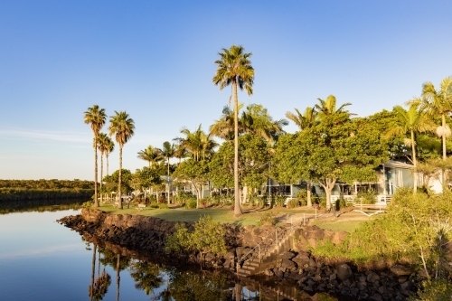 Caravan park beside Brunswick River with tall palm trees reflected in water - Australian Stock Image