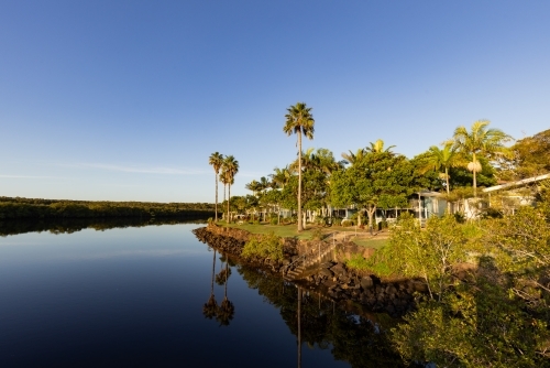 Caravan park beside Brunswick River with tall palm trees reflected in water - Australian Stock Image