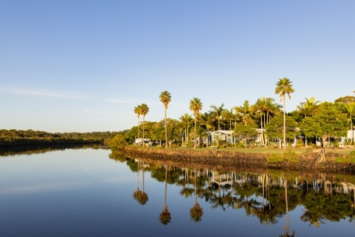 Caravan park beside Brunswick River with tall palm trees reflected in water - Australian Stock Image