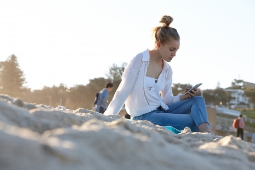 Carefree young blonde-haired woman at beach checking mobile phone