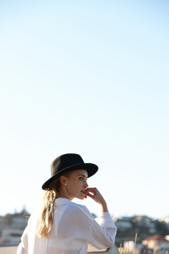 Carefree young blonde-haired woman at beach wearing black hat - Australian Stock Image