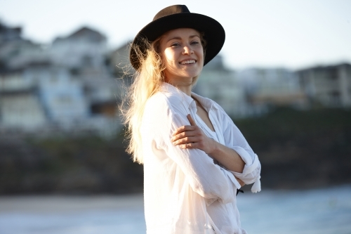 Carefree young blonde-haired woman at beach wearing black hat - Australian Stock Image