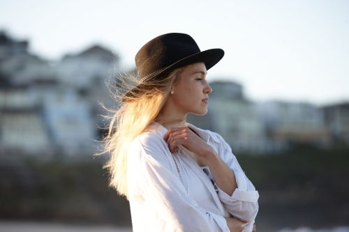 Carefree young blonde-haired woman at beach wearing black hat - Australian Stock Image