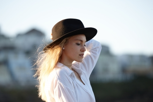 Carefree young blonde-haired woman at beach wearing black hat - Australian Stock Image