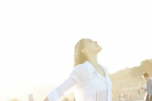 Carefree young blonde-haired woman at beach with arms out-stretched enjoying the sunshine - Australian Stock Image