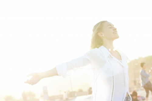 Carefree young blonde-haired woman at beach with arms out-stretched enjoying the sunshine - Australian Stock Image