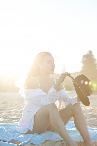 Carefree young blonde-haired woman at beach with black hat - Australian Stock Image