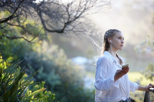 Carefree young blonde-haired woman listening to music with headphones outdoors - Australian Stock Image