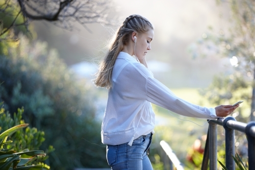 Carefree young blonde-haired woman listening to music with headphones outdoors - Australian Stock Image