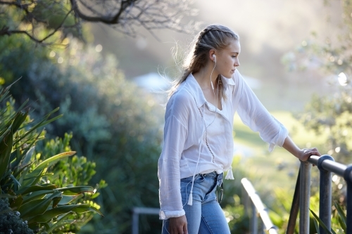 Carefree young blonde-haired woman listening to music with headphones outdoors - Australian Stock Image