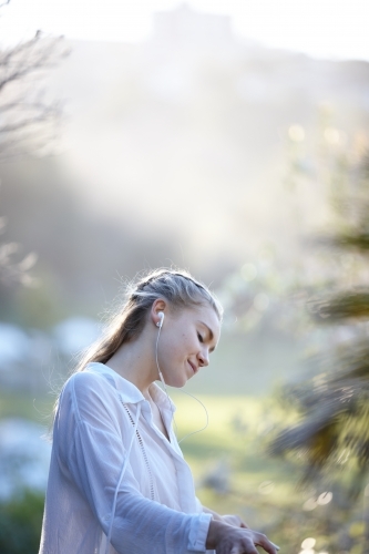 Carefree young blonde-haired woman listening to music with headphones outdoors - Australian Stock Image