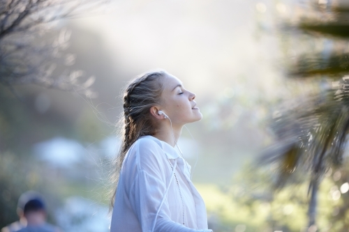 Carefree young blonde-haired woman listening to music with headphones outdoors - Australian Stock Image