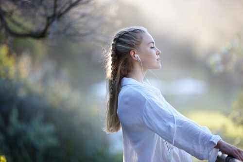 Carefree young blonde-haired woman listening to music with headphones outdoors - Australian Stock Image