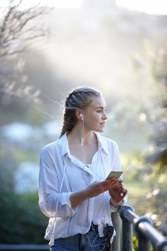 Carefree young blonde-haired woman listening to music with headphones outdoors - Australian Stock Image