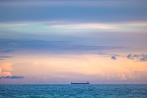 Cargo ship lined up at sea en route to Newcastle Harbour under a vibrant sunset sky - Australian Stock Image