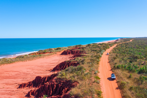 Cars driving on remote red dirt road by the sea - Australian Stock Image