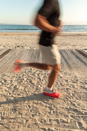 Caucasian male jogging on sandy boardwalk at beach - Australian Stock Image