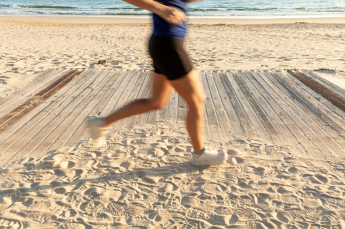 Caucasian woman jogging on sandy beach boardwalk - Australian Stock Image