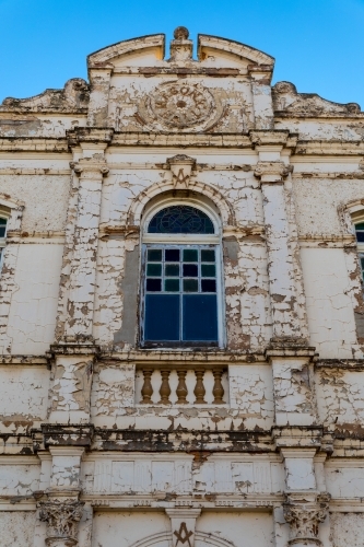 Center window of an old derelict building with weathered facade standing grand against a blue sky